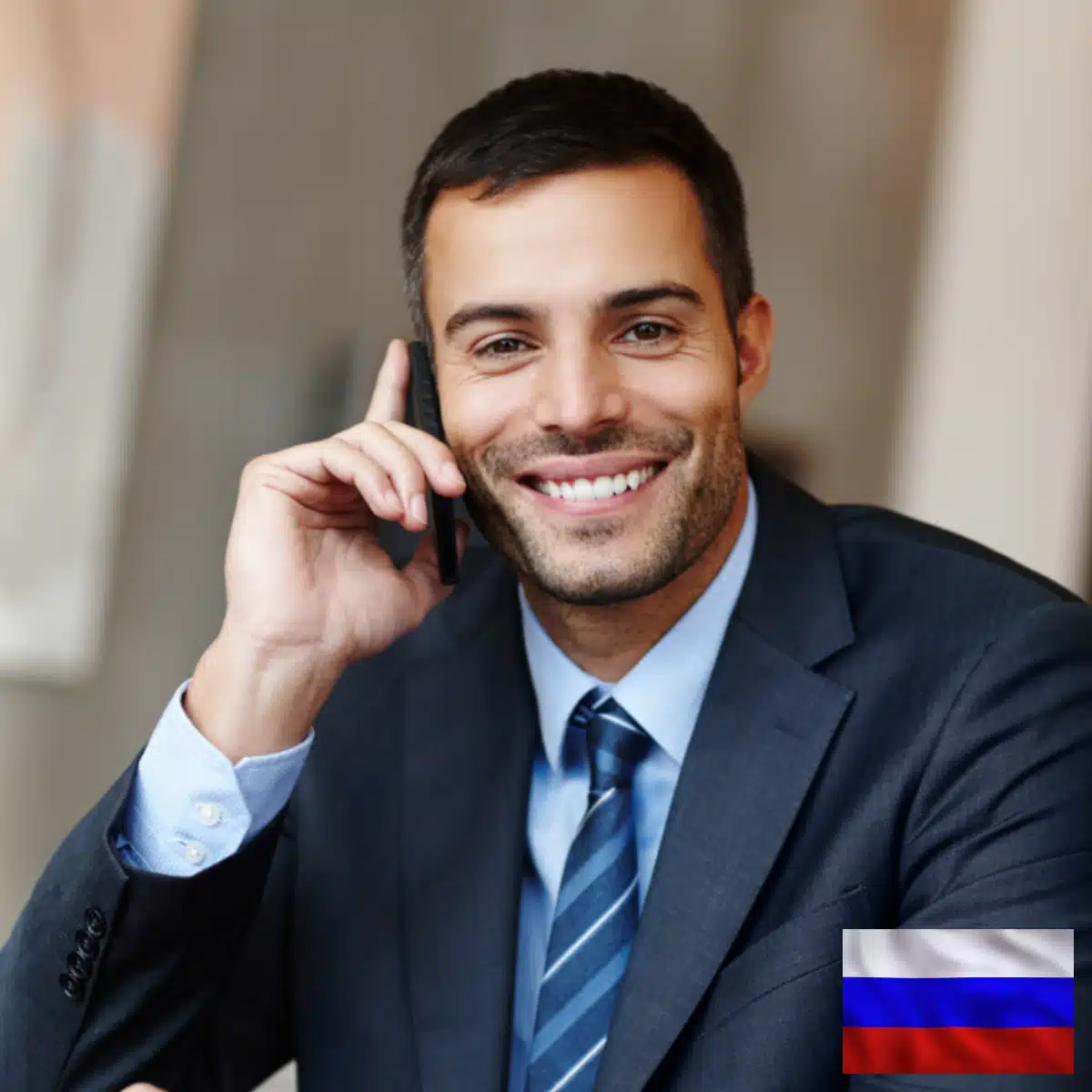 A man in a dark suit and tie smiles while talking on a mobile phone. There is a small Russian flag icon in the bottom right corner of the image.
